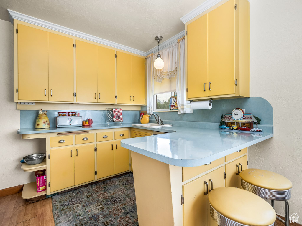 Kitchen with a peninsula, wood finished floors, light countertops, a kitchen breakfast bar, and decorative light fixtures