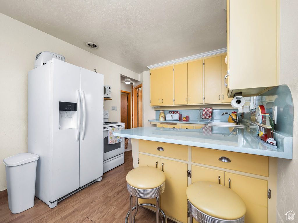 Kitchen with white appliances, a peninsula, light wood-style flooring, light countertops, and cream cabinetry