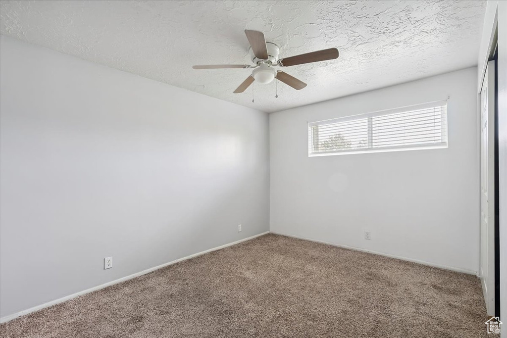 Carpeted empty room with ceiling fan and a textured ceiling