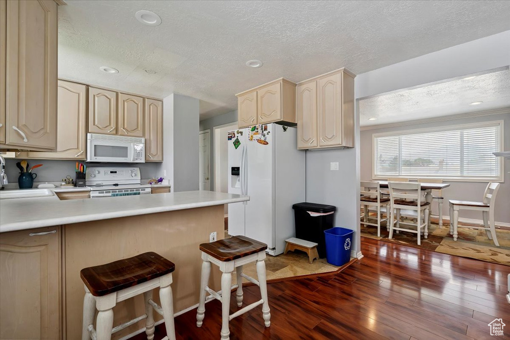 Kitchen featuring white appliances, a textured ceiling, dark wood-style floors, a peninsula, and light countertops