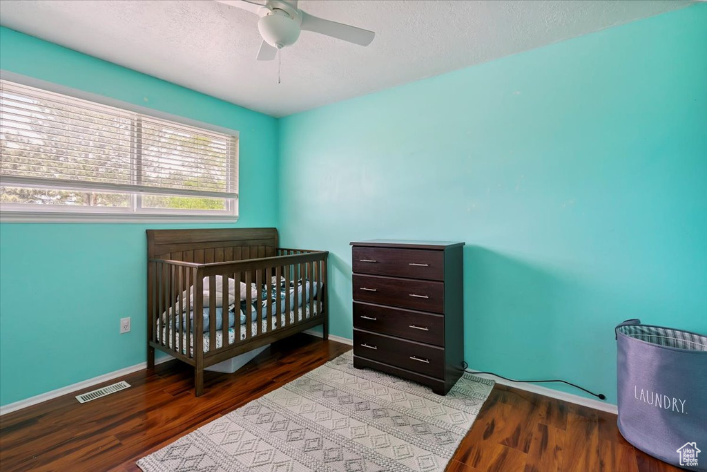Bedroom featuring wood finished floors, a textured ceiling, a ceiling fan, and a crib