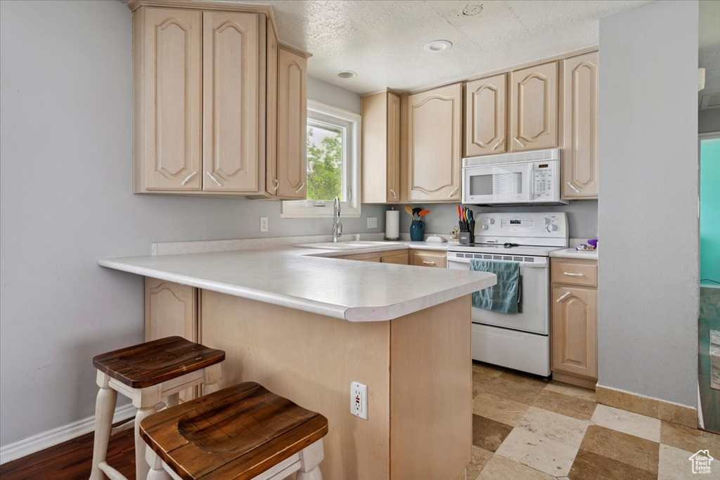 Kitchen featuring white appliances, light brown cabinets, a peninsula, a kitchen breakfast bar, and light countertops