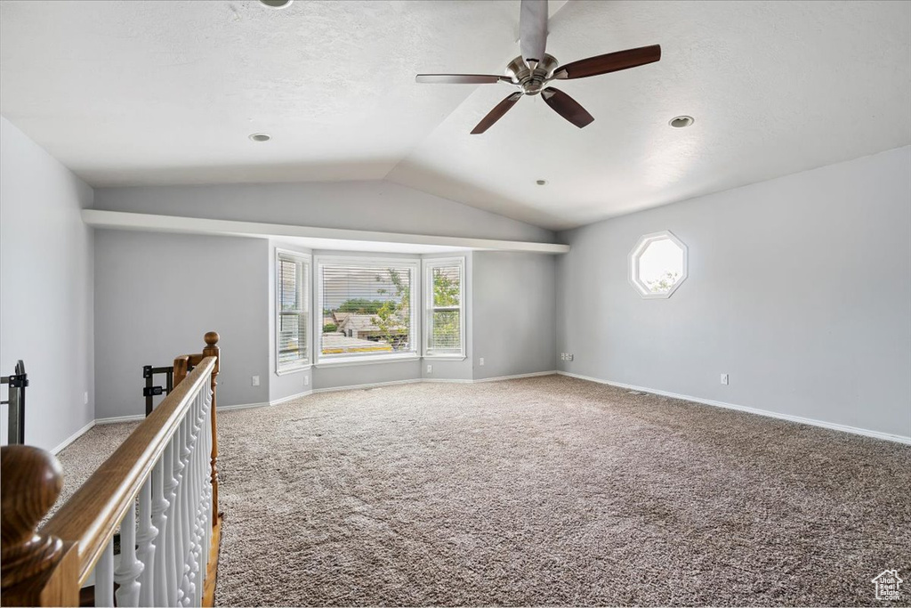 Carpeted empty room with a ceiling fan and vaulted ceiling
