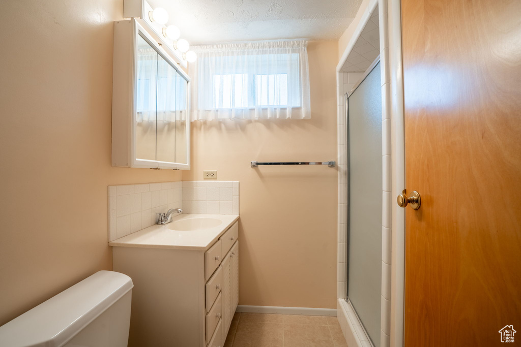 Bathroom featuring vanity, a shower with door, decorative backsplash, and tile patterned floors