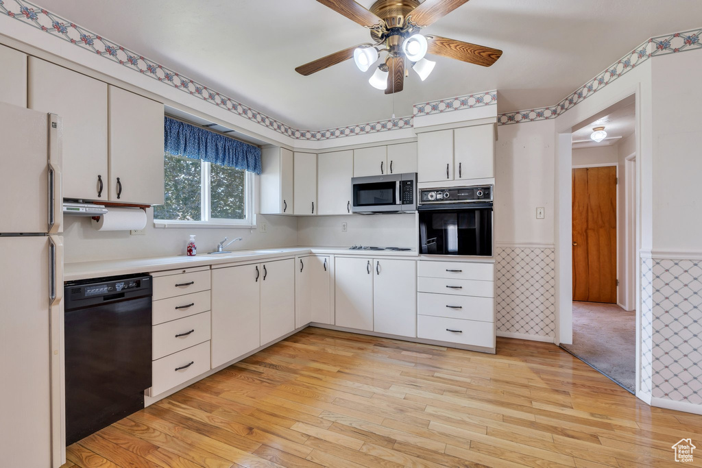 Kitchen featuring black appliances, light countertops, light wood finished floors, wainscoting, and a ceiling fan
