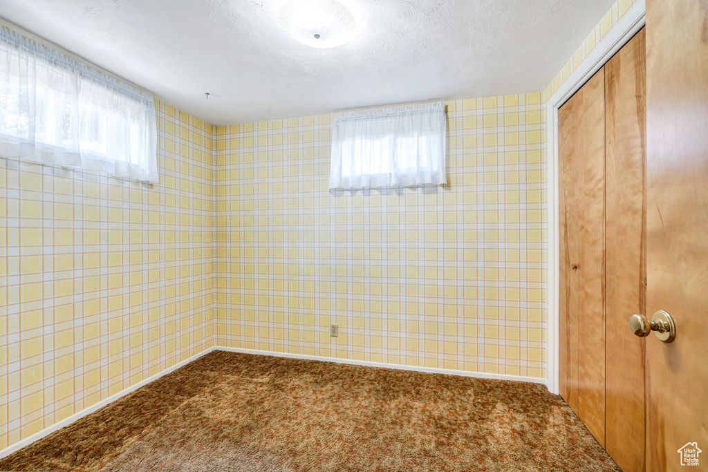 Unfurnished bedroom featuring a closet, dark carpet, wallpapered walls, and a textured ceiling
