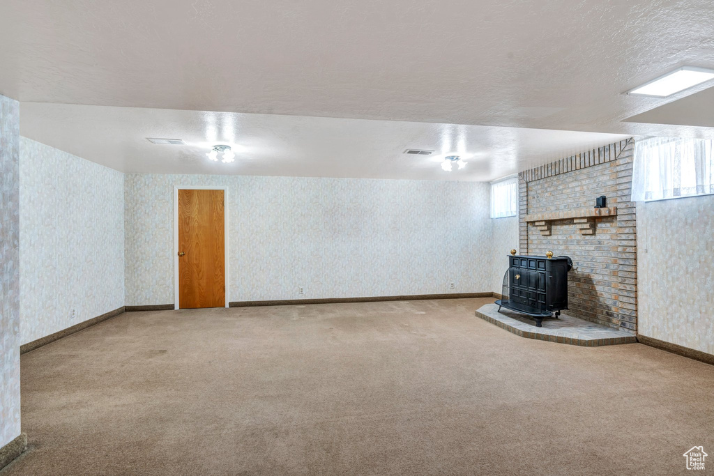 Basement with a wood stove, carpet flooring, wallpapered walls, and a textured ceiling