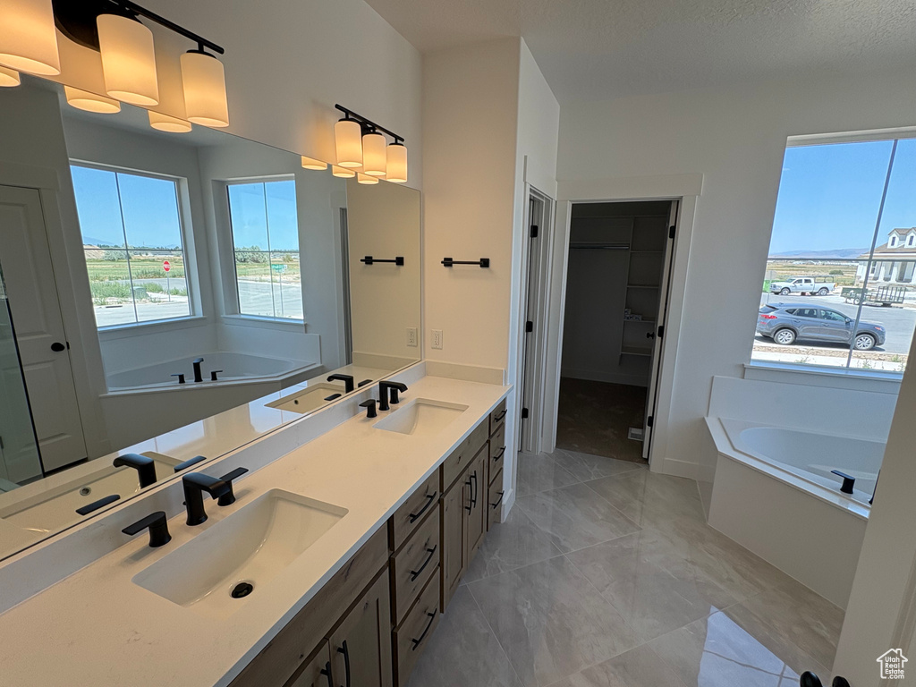Full bath featuring a bath, double vanity, marble look tiles, and a walk in closet