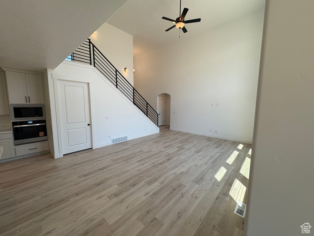 Unfurnished living room with light wood-style floors, stairway, arched walkways, a ceiling fan, and a towering ceiling