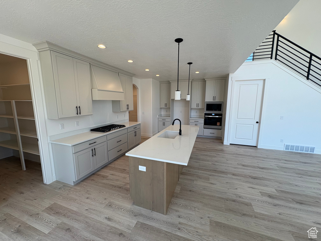 Kitchen with appliances with stainless steel finishes, gray cabinetry, light wood finished floors, arched walkways, and recessed lighting