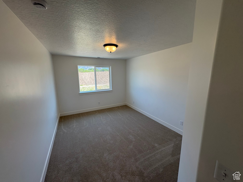 Empty room with dark colored carpet, a smoke detector, and a textured ceiling