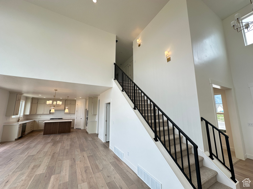 Stairway with a towering ceiling, a chandelier, wood finished floors, healthy amount of natural light, and recessed lighting