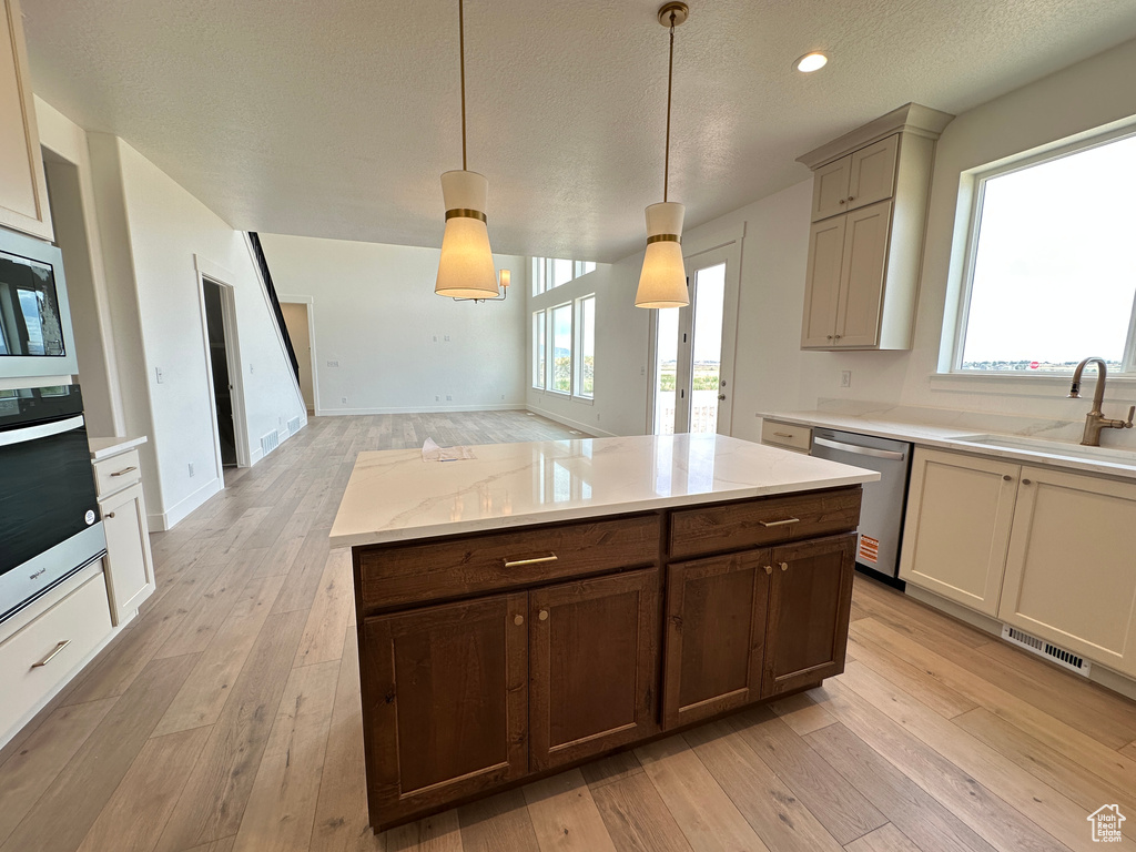 Kitchen with appliances with stainless steel finishes, light wood-type flooring, decorative light fixtures, a textured ceiling, and recessed lighting