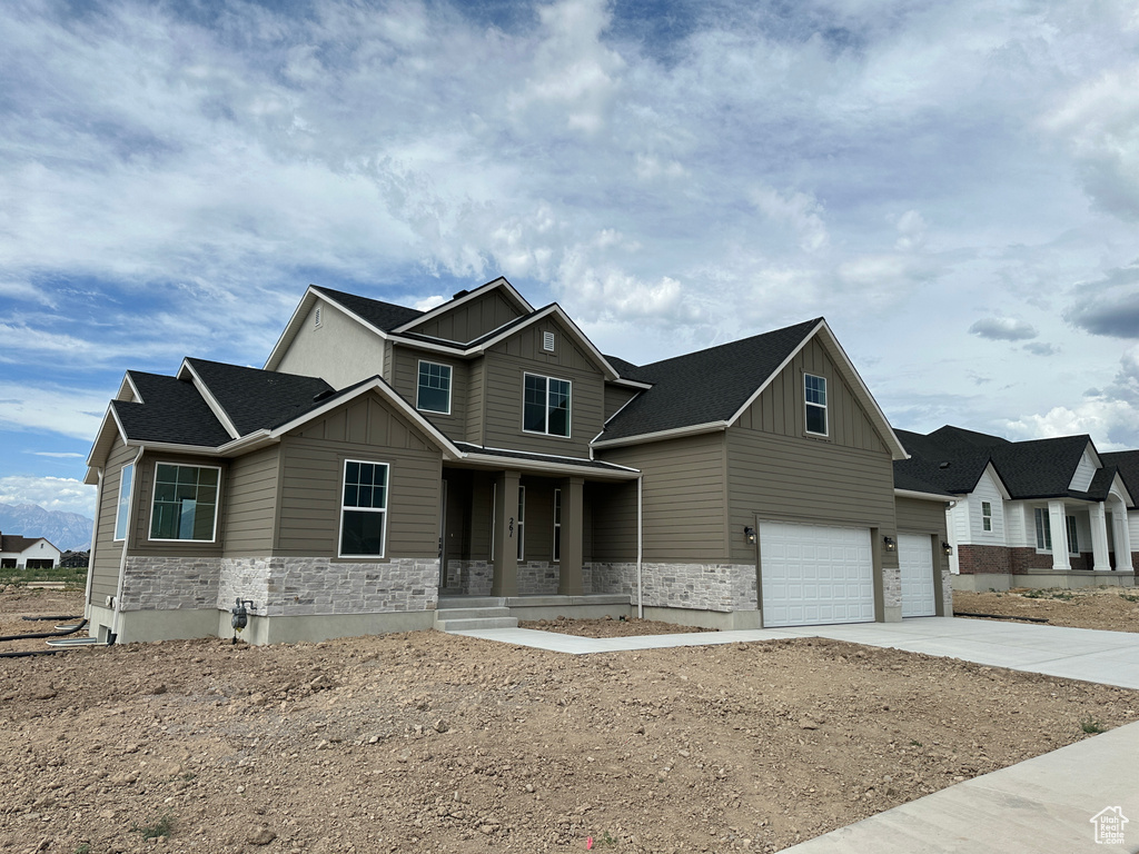 Craftsman house featuring board and batten siding, stone siding, an attached garage, and covered porch
