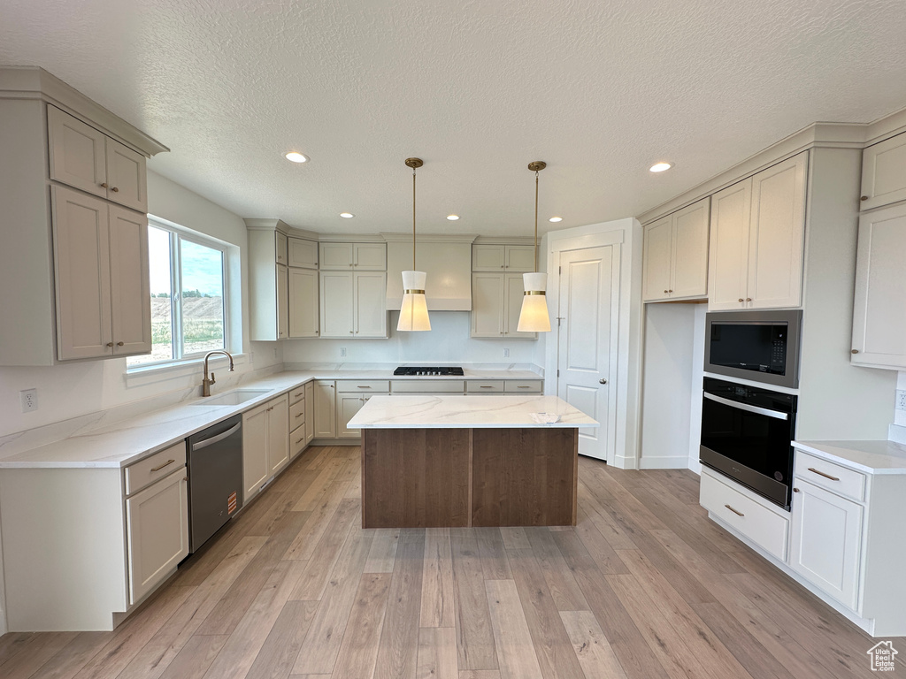 Kitchen featuring black appliances, light wood finished floors, a center island, recessed lighting, and pendant lighting