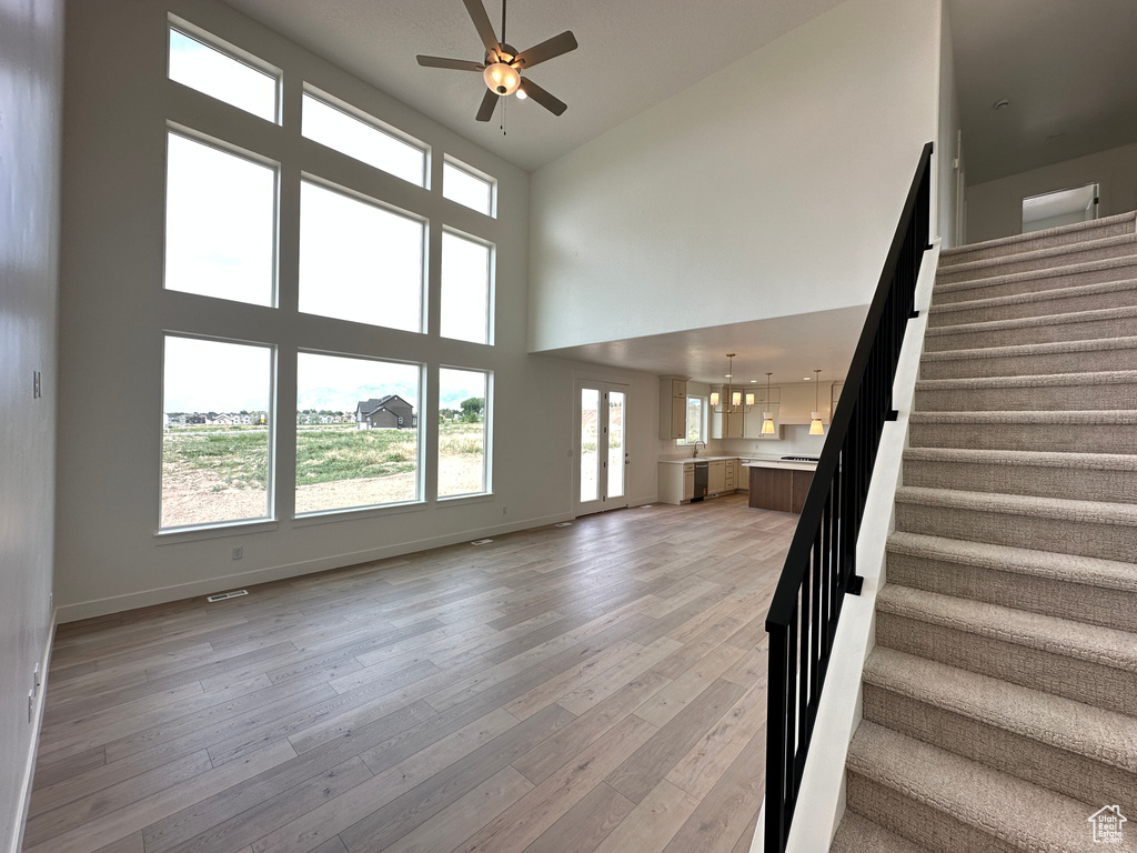 Unfurnished living room featuring a high ceiling, stairs, ceiling fan, light wood-style flooring, and plenty of natural light
