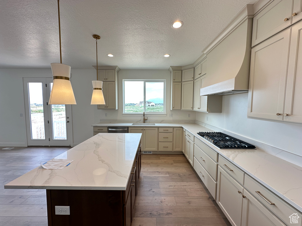 Kitchen featuring appliances with stainless steel finishes, a textured ceiling, custom range hood, light wood-type flooring, and a center island