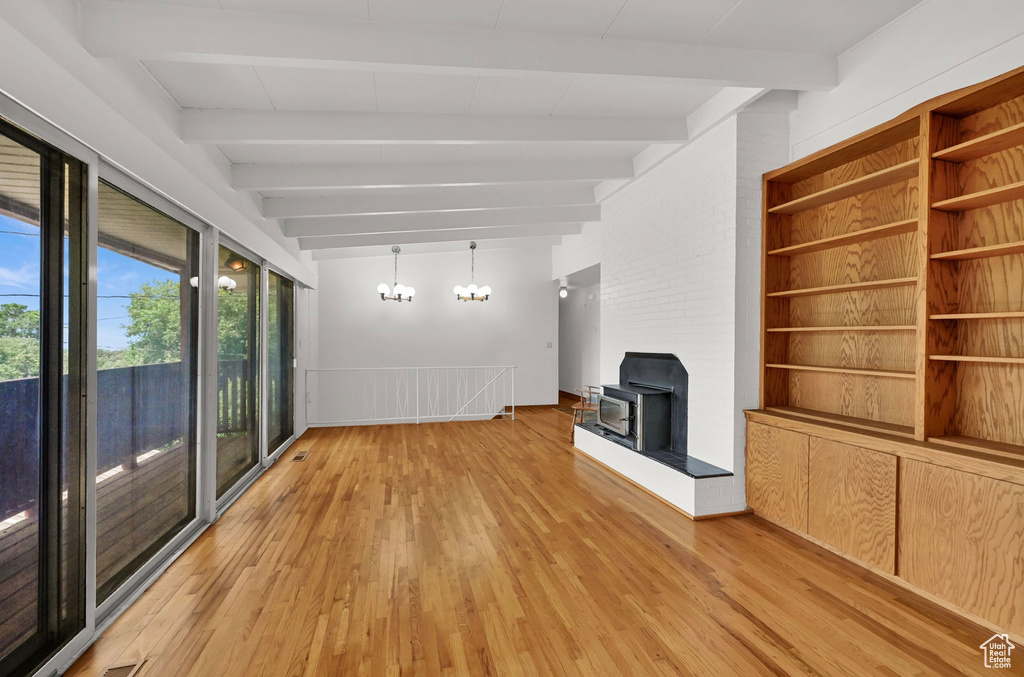 Unfurnished living room with a wood stove, beam ceiling, light wood-style floors, and a chandelier