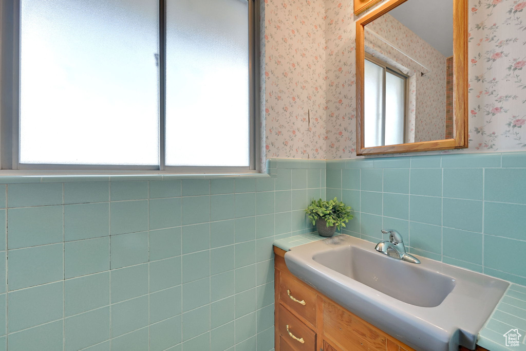 Bathroom featuring wallpapered walls, vanity, a wainscoted wall, and tile walls
