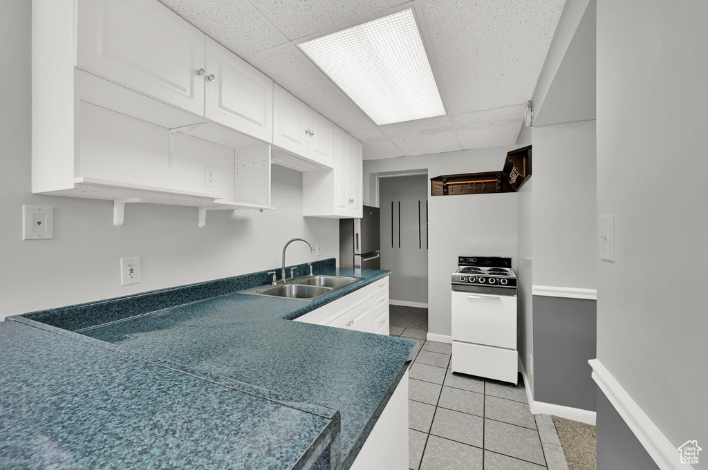 Kitchen featuring white range with electric cooktop, white cabinetry, light tile patterned floors, dark countertops, and a drop ceiling