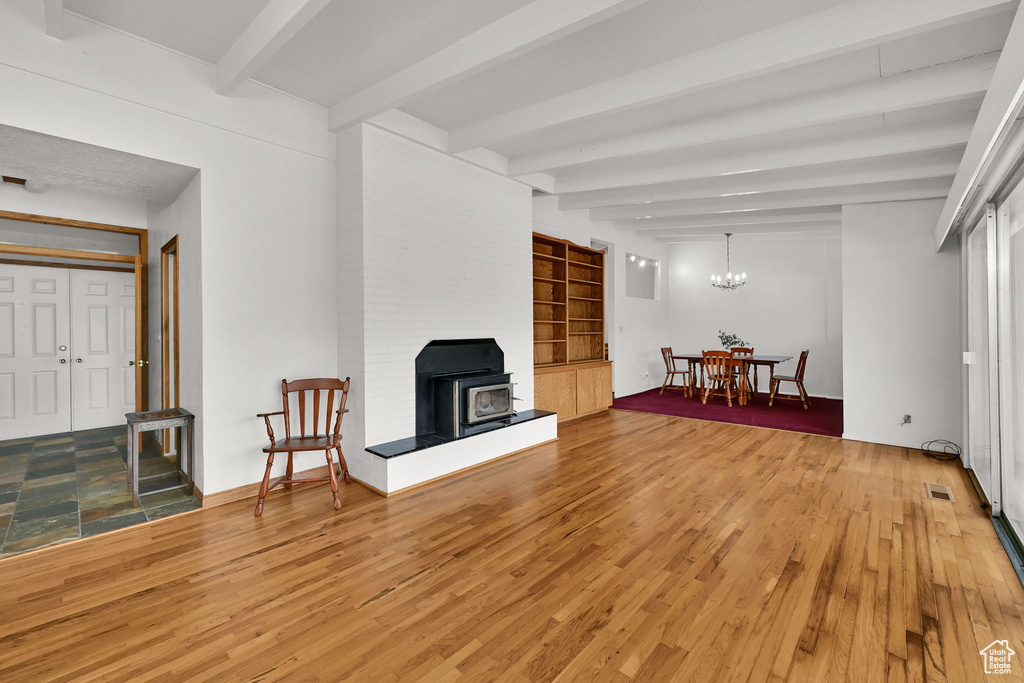 Living room featuring beam ceiling, light wood-style flooring, a wood stove, and a chandelier
