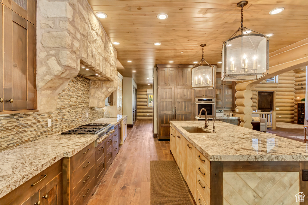 Kitchen featuring rustic walls, appliances with stainless steel finishes, light wood-style flooring, wooden ceiling, and light stone counters
