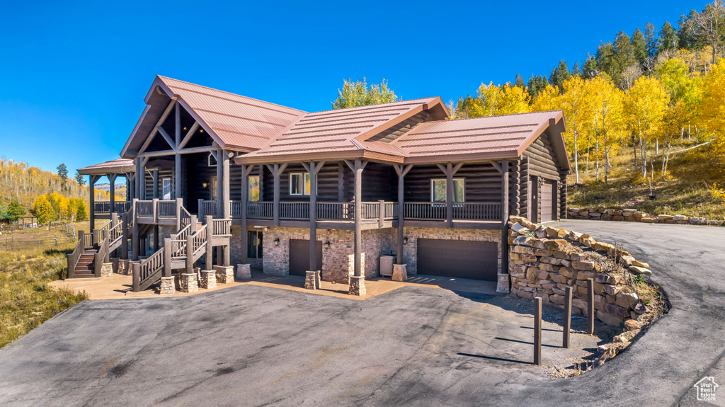 Log-style house featuring a garage, log exterior, stairs, stone siding, and a balcony