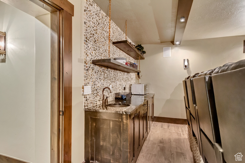 Kitchen featuring open shelves, light wood-style flooring, white microwave, stone counters, and backsplash