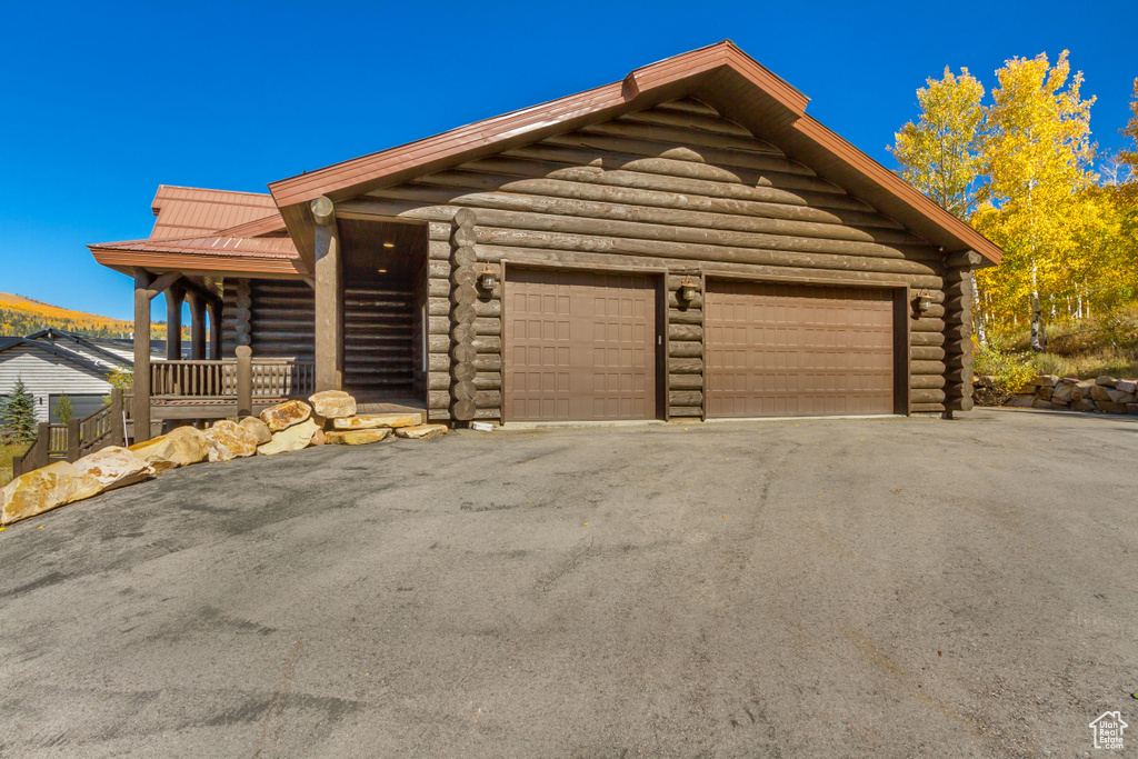 View of front of house featuring log siding, a garage, driveway, and a metal roof