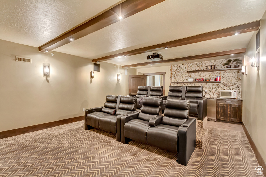 Cinema room featuring beam ceiling, light colored carpet, and a textured ceiling