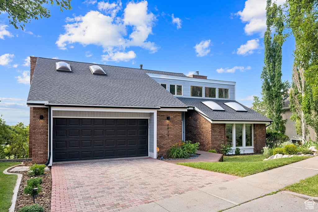 Mid-century home with brick siding, decorative driveway, roof with shingles, and an attached garage
