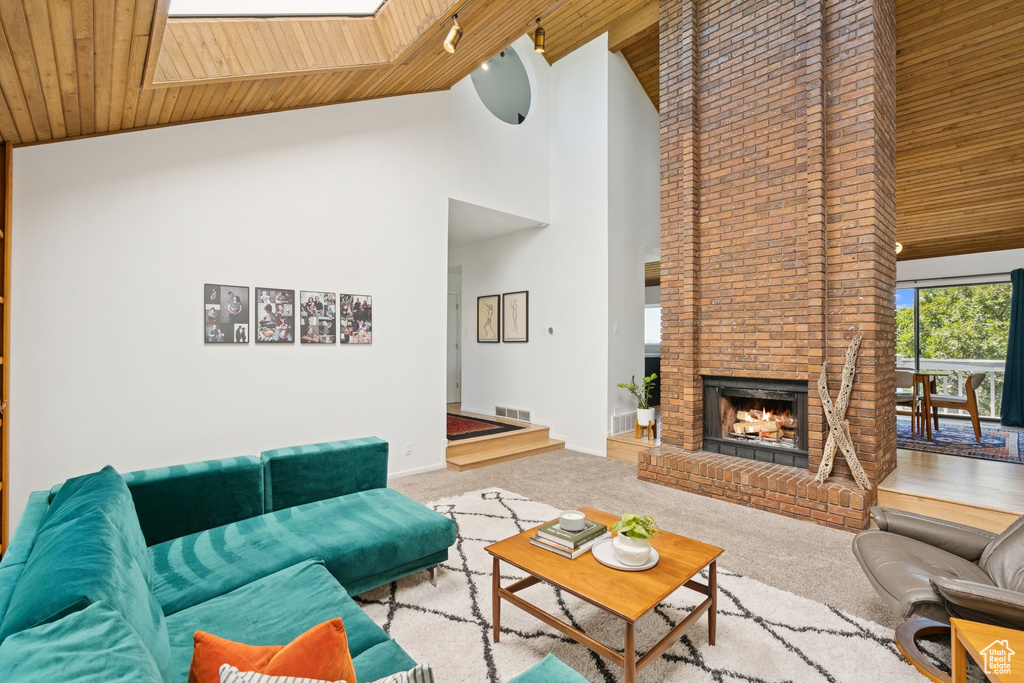 Carpeted living area featuring high vaulted ceiling, wood ceiling, a brick fireplace, and a skylight