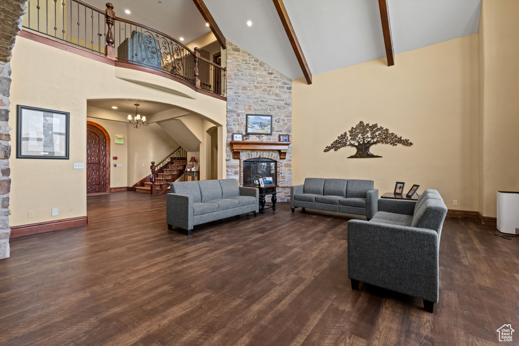 Living area featuring arched walkways, high vaulted ceiling, stairs, a stone fireplace, and dark wood-style floors