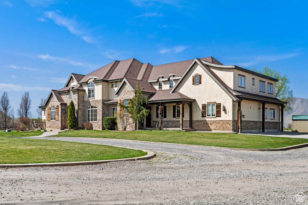 French country style house featuring stucco siding, curved driveway, stone siding, and a front yard