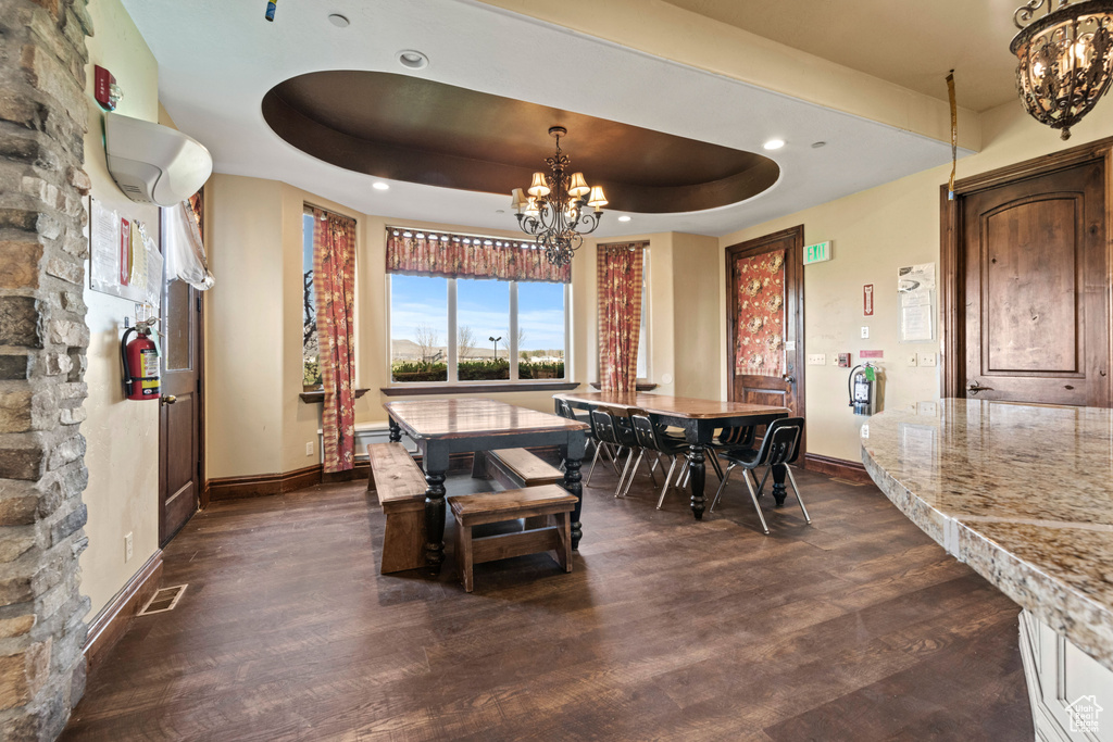 Dining space with a chandelier, dark wood-type flooring, a raised ceiling, and recessed lighting