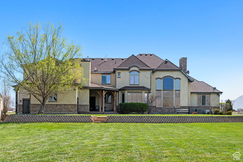 View of front of property featuring stucco siding, a front yard, a chimney, and stone siding