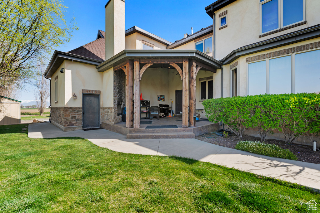 Back of property with stucco siding, a lawn, a chimney, and stone siding