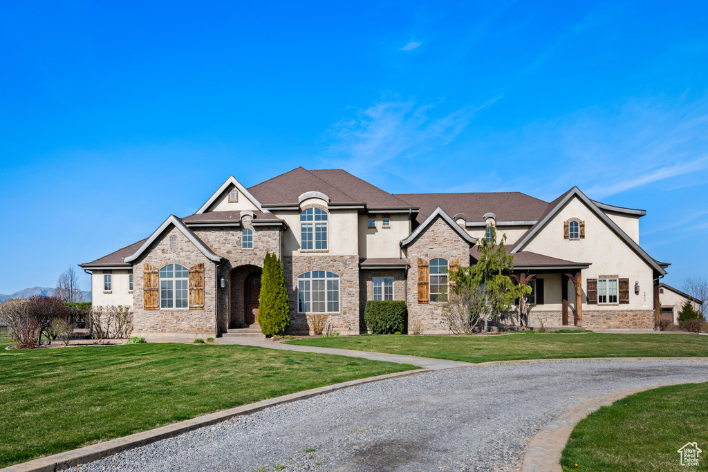 French country home with stucco siding, a front lawn, and stone siding