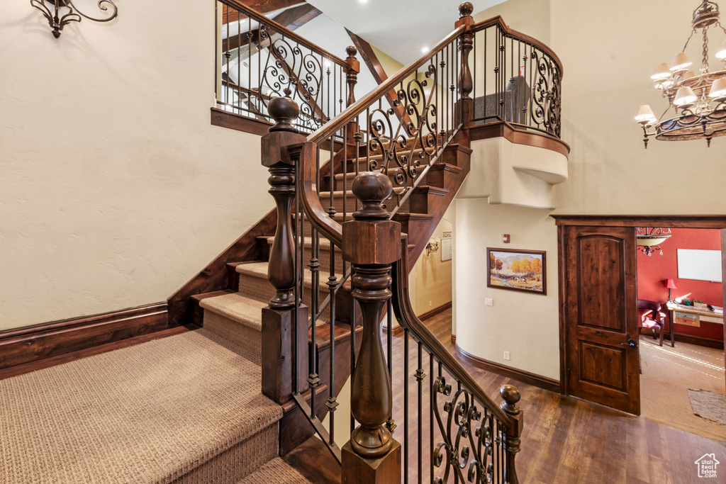 Stairs with a chandelier, wood finished floors, and a towering ceiling