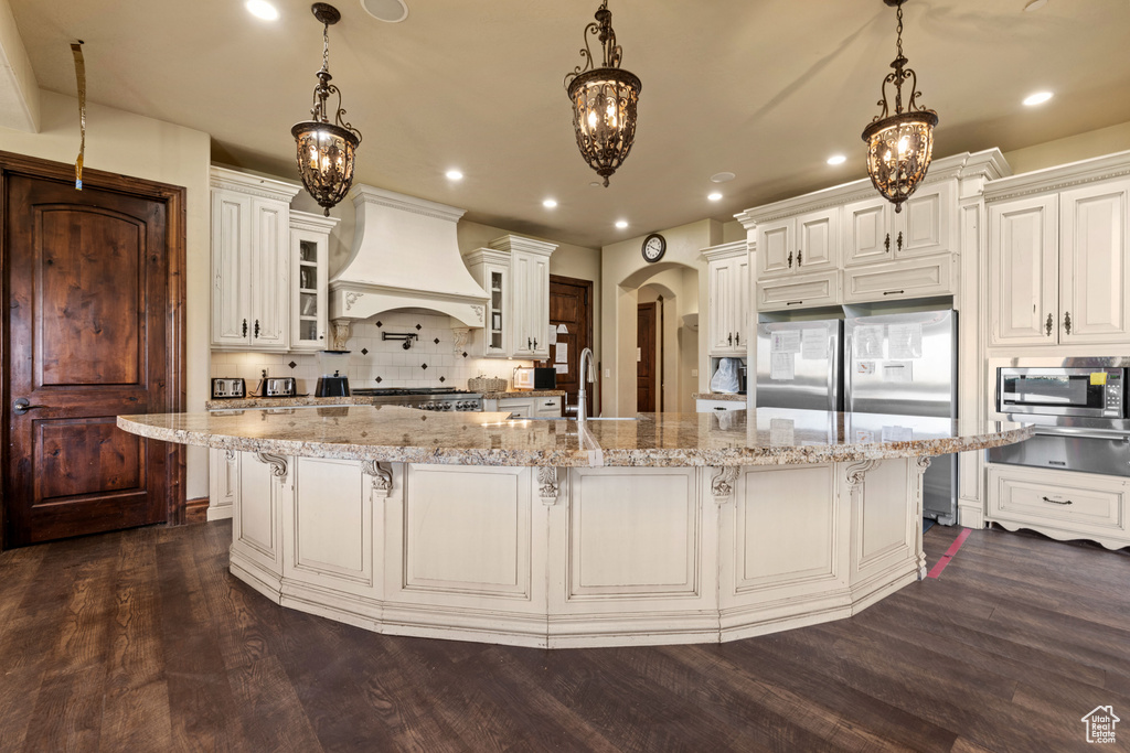 Kitchen featuring custom exhaust hood, appliances with stainless steel finishes, a warming drawer, arched walkways, and dark wood-type flooring