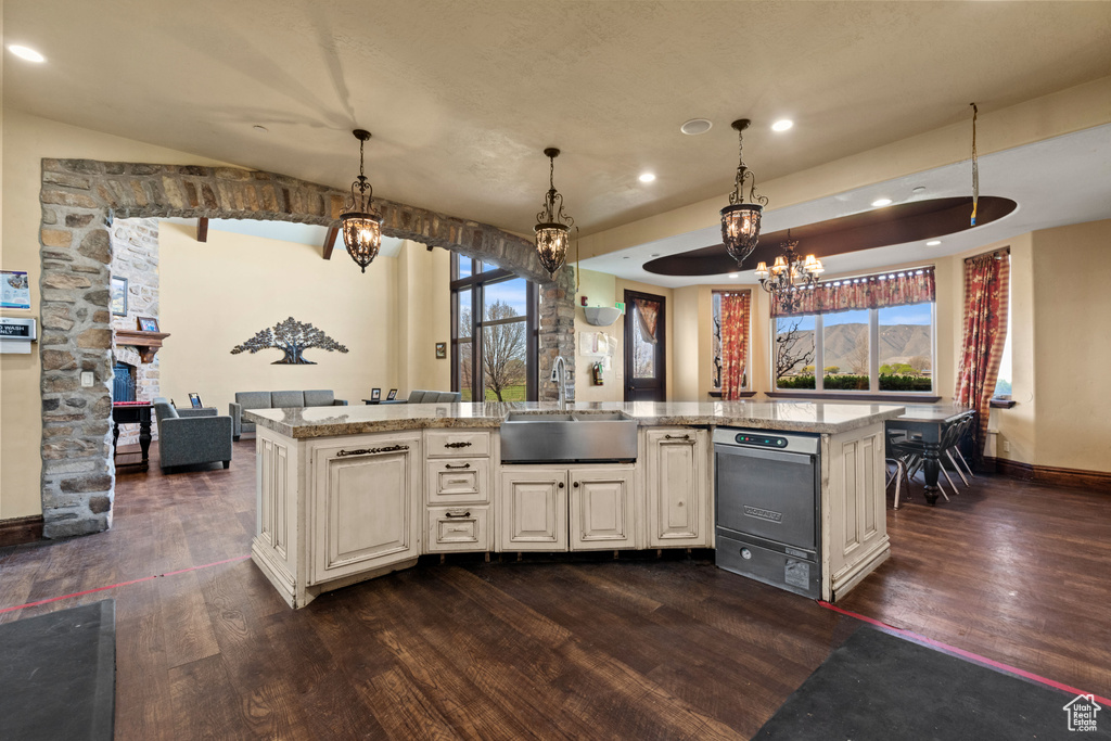 Kitchen featuring dark wood-style flooring, a chandelier, dishwashing machine, light stone countertops, and healthy amount of natural light