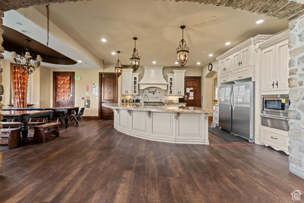 Kitchen featuring appliances with stainless steel finishes, premium range hood, a warming drawer, a chandelier, and dark wood finished floors
