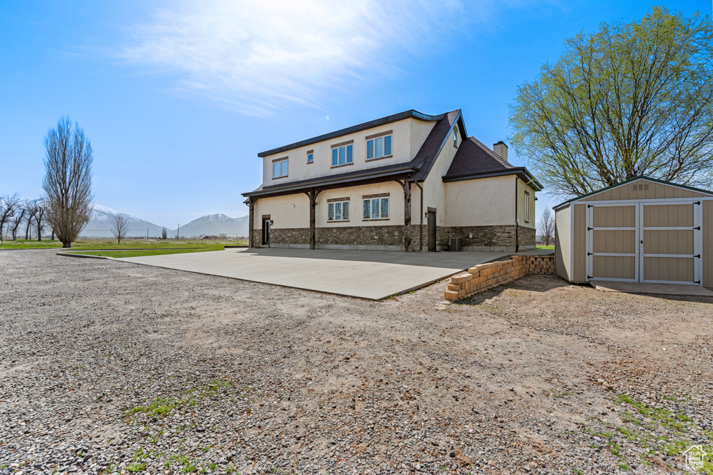Back of property featuring stucco siding, a storage shed, stone siding, a chimney, and a mountain view
