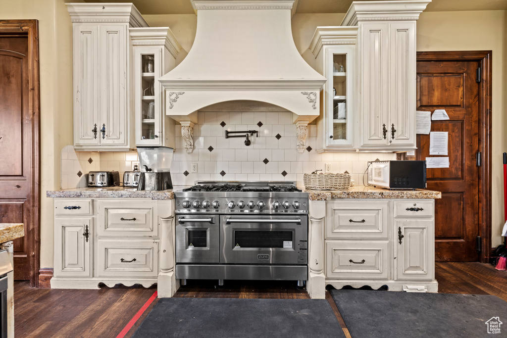 Kitchen featuring double oven range, premium range hood, dark wood-type flooring, and backsplash