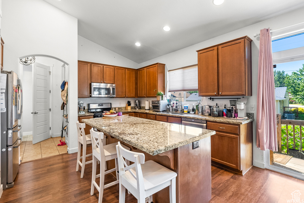 Kitchen featuring stainless steel appliances, lofted ceiling, a center island, a breakfast bar area, and brown cabinetry