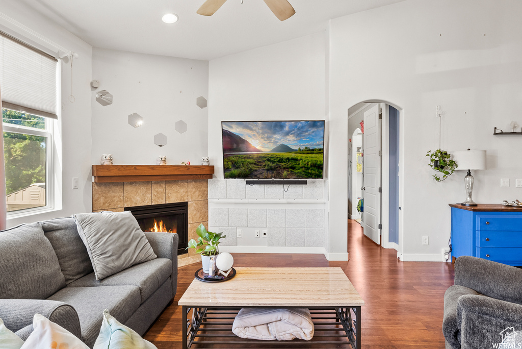 Living room featuring wood finished floors, arched walkways, a tiled fireplace, a ceiling fan, and recessed lighting