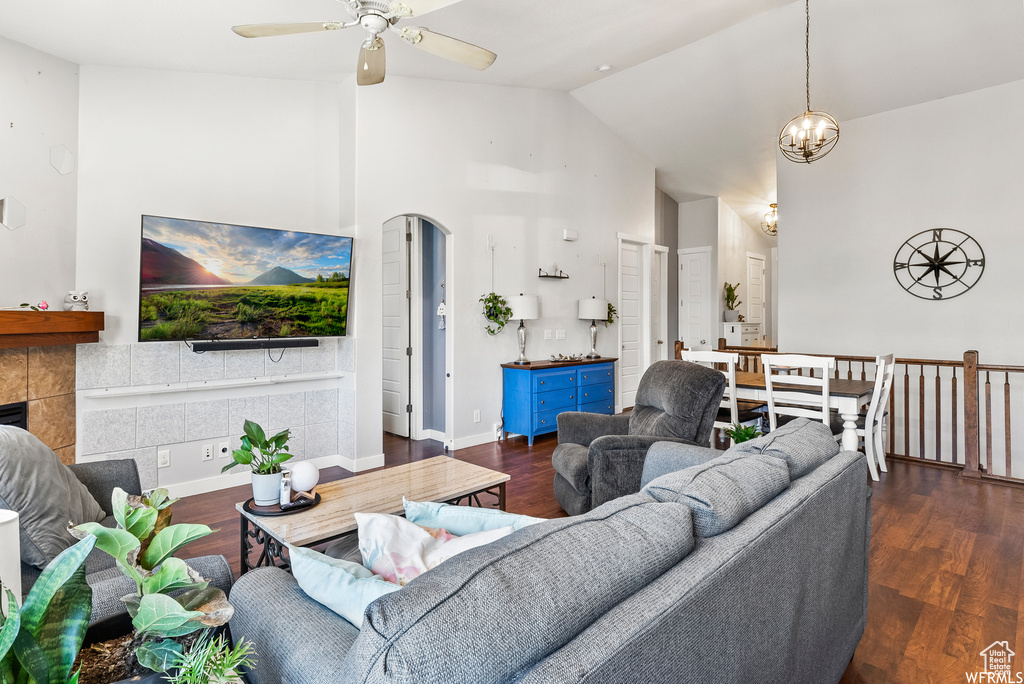 Living room with a ceiling fan, wood finished floors, a tiled fireplace, high vaulted ceiling, and a chandelier