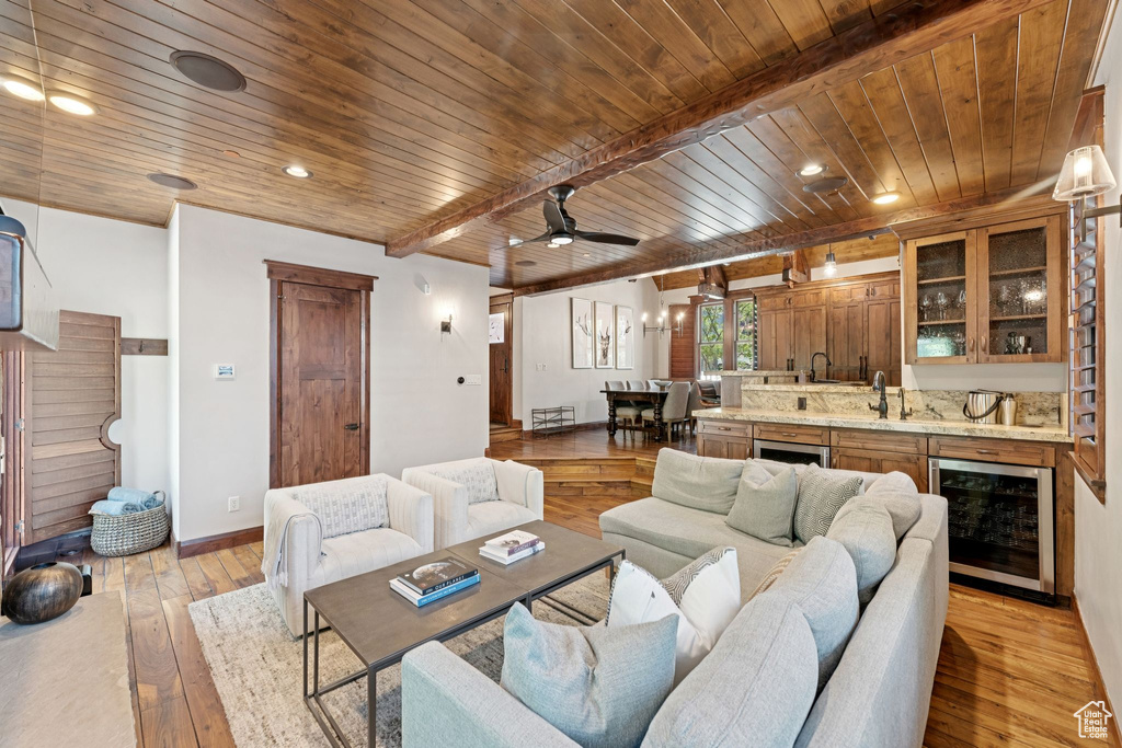 Living room featuring beverage cooler, wooden ceiling, light wood-style flooring, bar with sink, and a ceiling fan