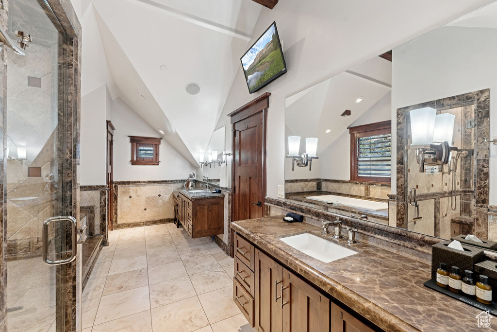 Bathroom featuring vaulted ceiling, two vanities, a shower stall, a garden tub, and a wainscoted wall