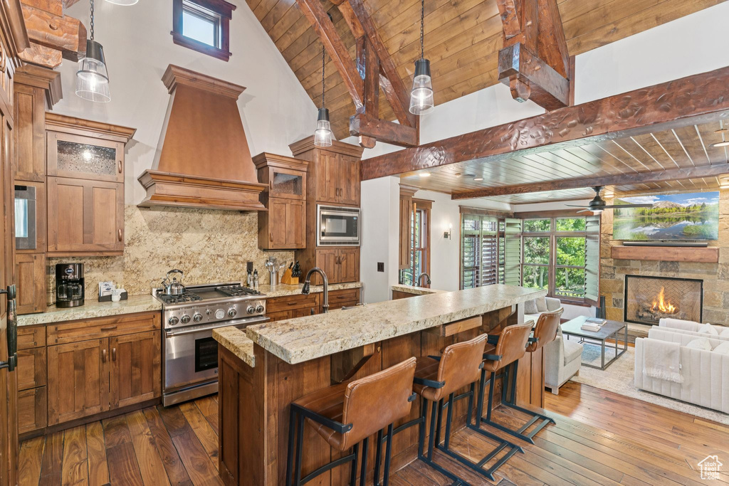 Kitchen featuring appliances with stainless steel finishes, premium range hood, a wood ceiling with exposed beams, open floor plan, and brown cabinetry